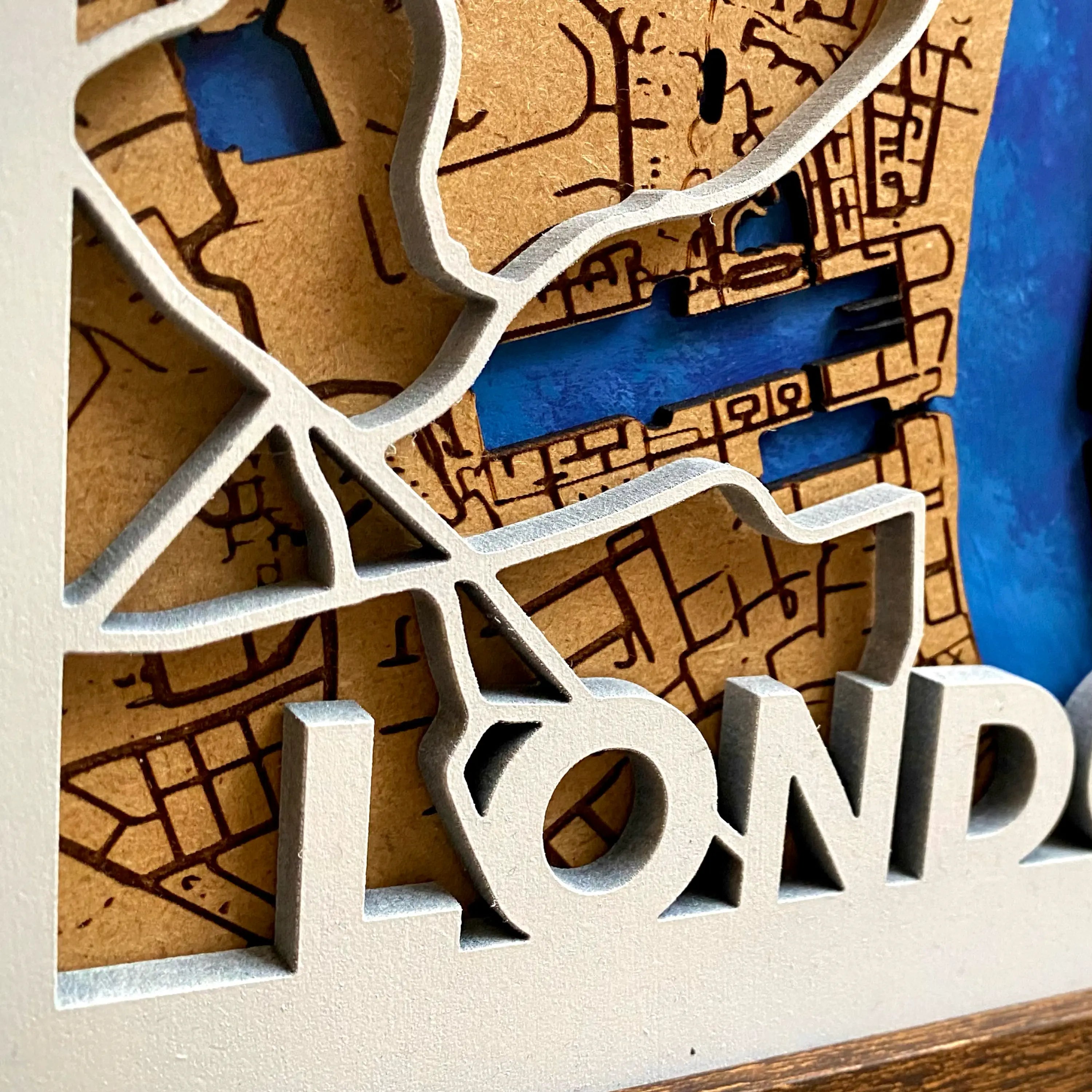 A closer look at the 3D laser-cut MDF letters of LONDON that are hand-painted in white on the bottom left hand corner of the frame. These letters are 3D and connect with the main roads/motorways layer of the wooden map.