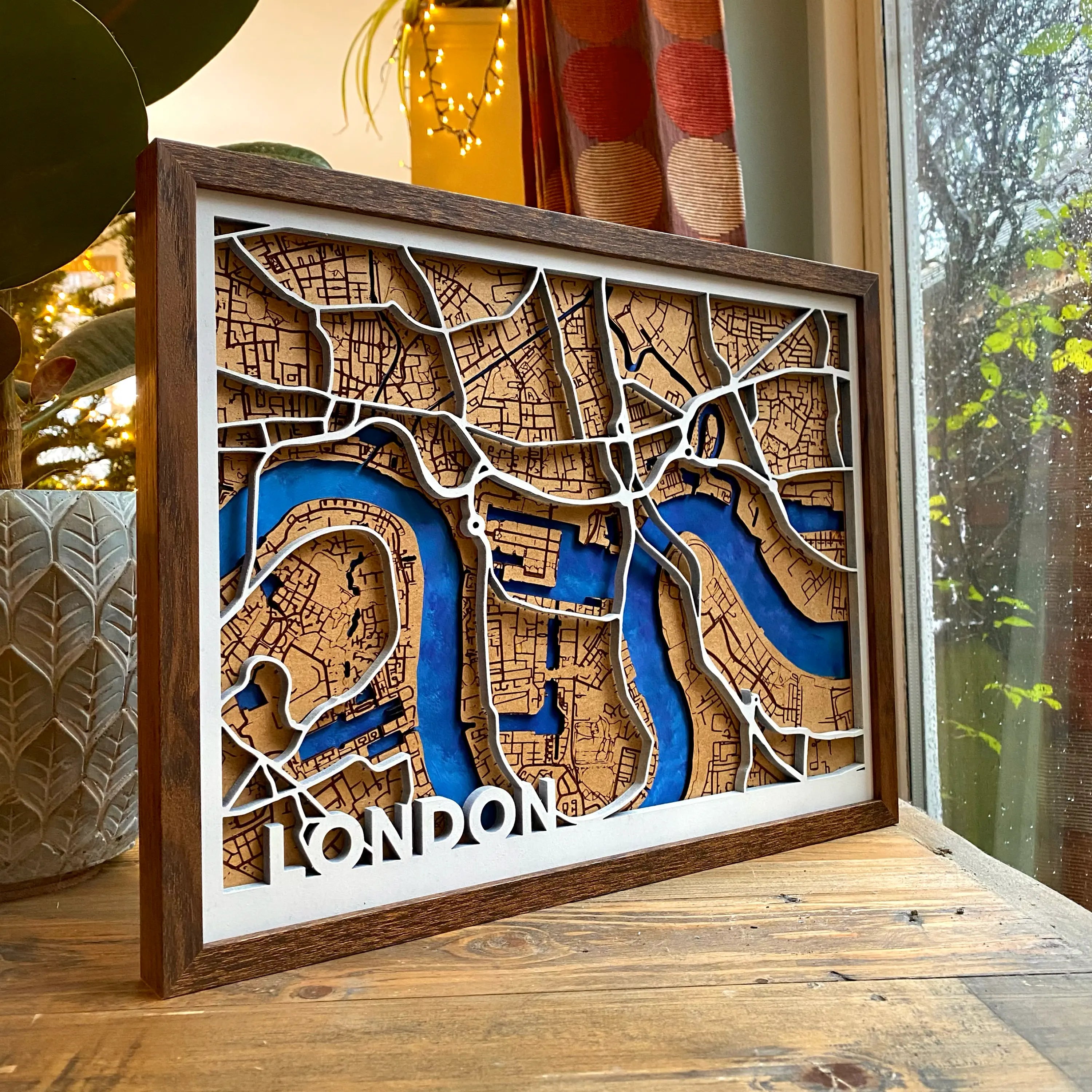 A beautiful shot of a wooden map in a dark birch wood frame and white painted border. The wooden map is positioned on a coffee table by a large window