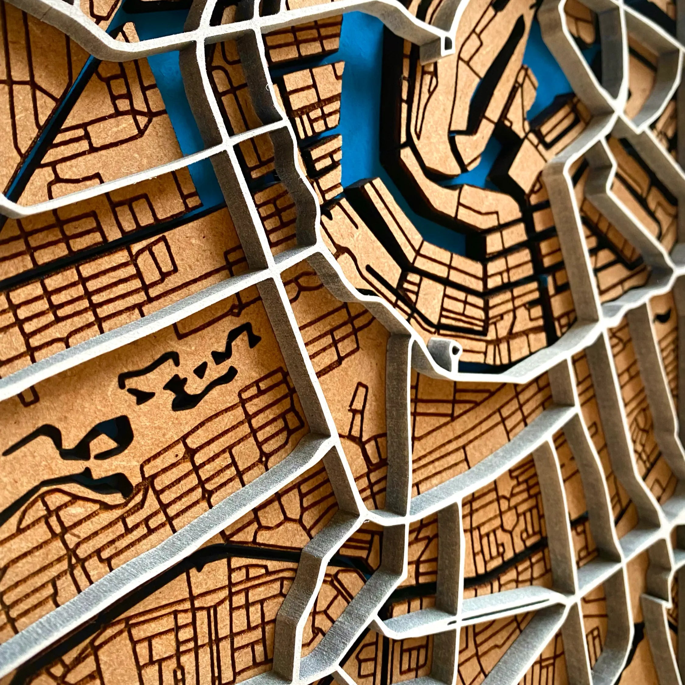 A close up of a vertical wooden map made using thick 6mm MDF of Amsterdam. The map is a 3D interpretation of Amsterdam city centre with elevated main roads and local streets, and painted blue rivers underneath